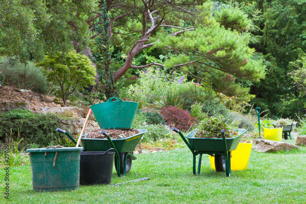 Gardening in a landscaped garden with wheelbarrows, buckets full of leaves and weeds.