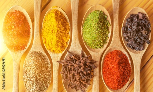 Various colorful spices in spoons on wooden table