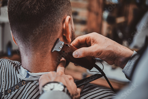 Thendy hairdresser at modern barbershop is working on client's haircut. Closeup photoshoot.