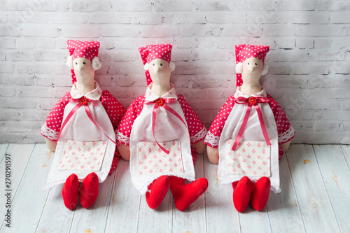 Three tilde dolls in red dresses, and white aprons, and red kalpaks sit on a light background. Interior dolls. There is a place for text. The concept of needlework,. photo