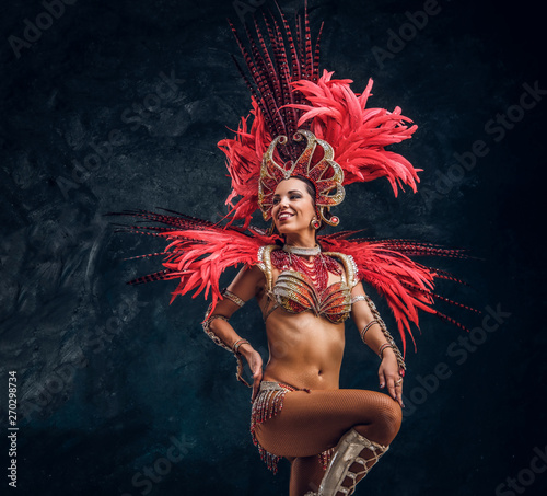 Young attractive brasil dancer in red feather costume is dancing at small dark studio. photo