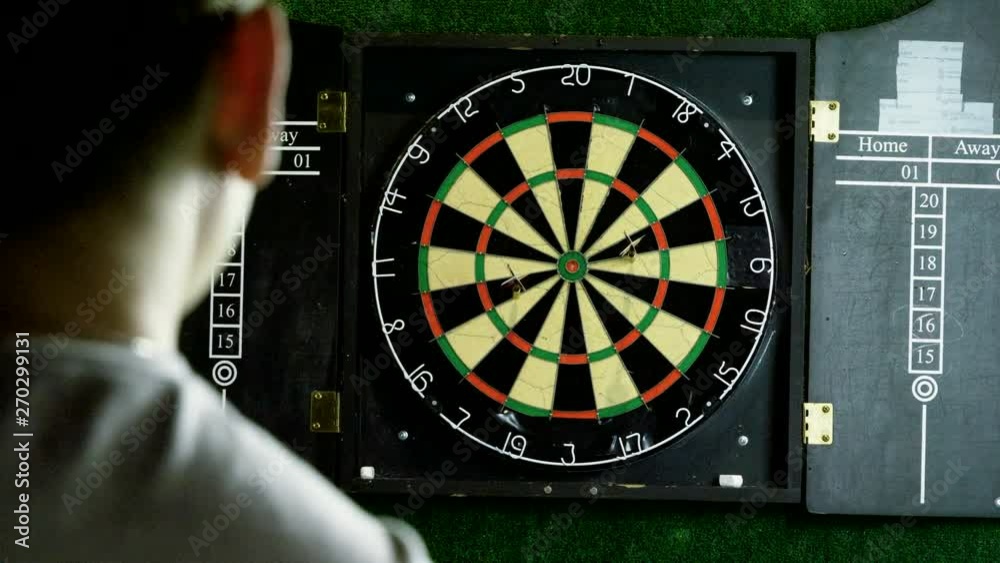 Man throwing a dart arrow in target center of dartboard in game of darts. 4K