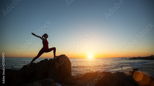 Silhouette young yoga woman doing fitness exercises on the sea beach at amazing sunset.