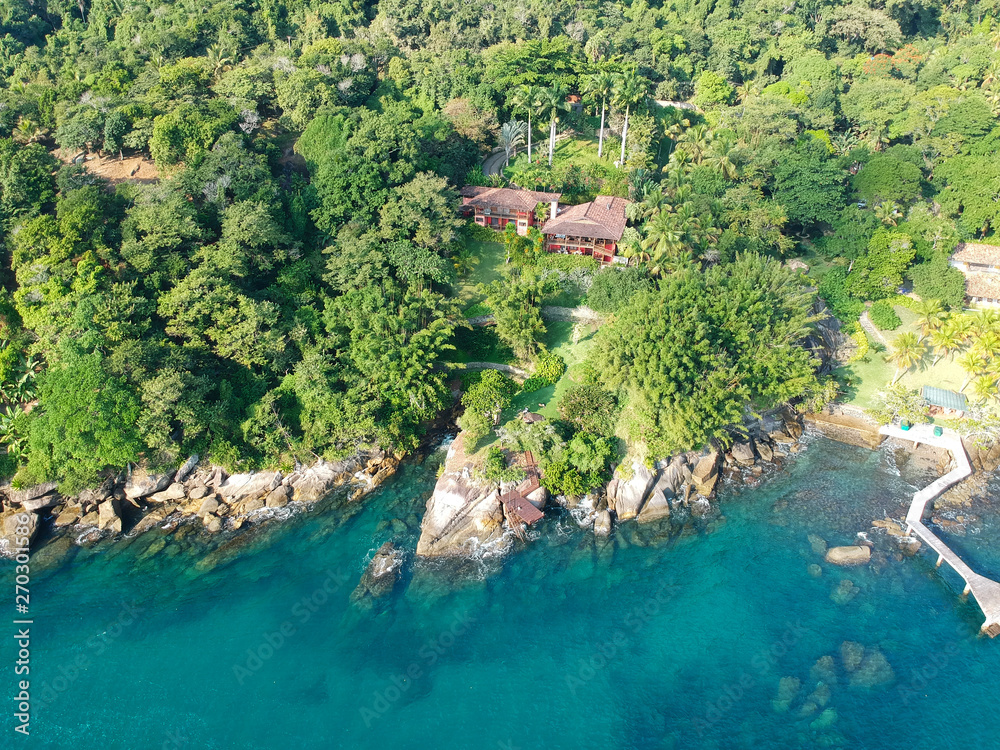 Aerial view of tropicsal house in forest surrounded by trees and next to the ocean and blue turquoise water. luxurious villa and spacious pavilion next to the sea, Brazil.