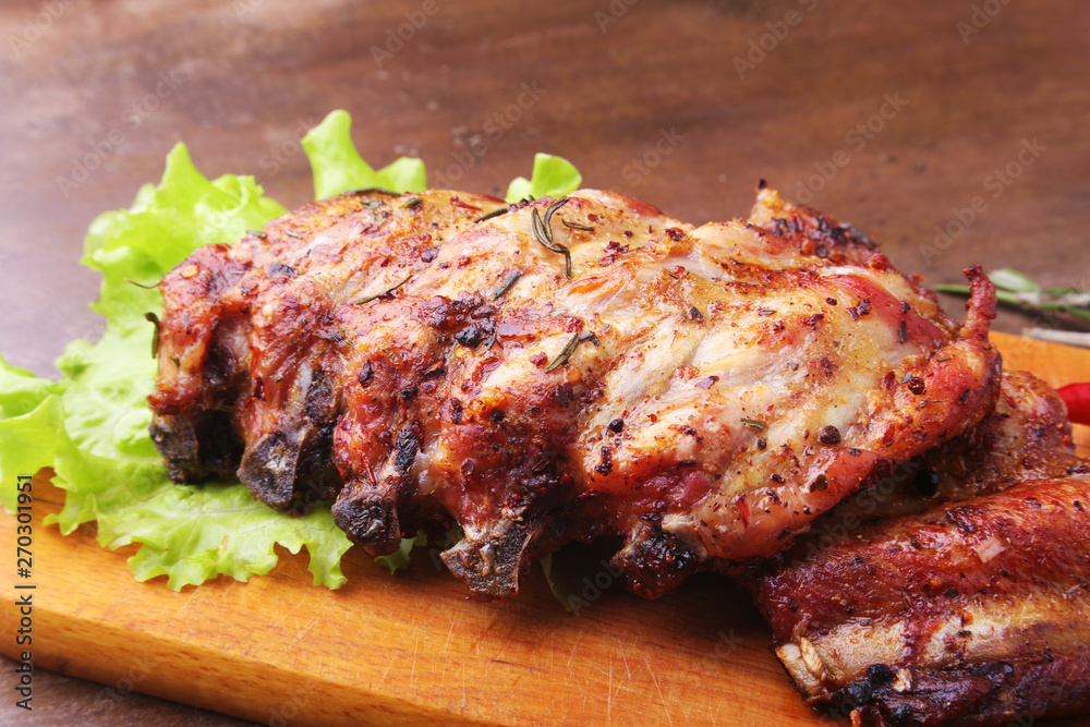 grilled barbecued ribs with lettuce leaves, hot chili pepper and sauce on wooden cutting board.