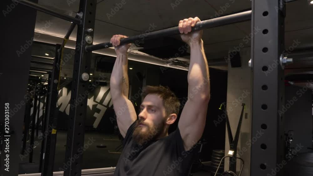 Closeup shoot of adult muscular athletic bodybuilder working out and lifting himself on the bars indoors in the gym