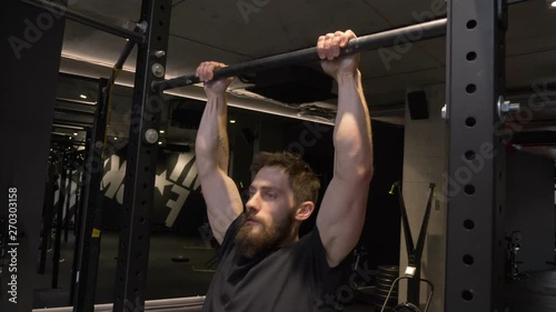 Closeup shoot of adult muscular athletic bodybuilder working out and lifting himself on the bars indoors in the gym