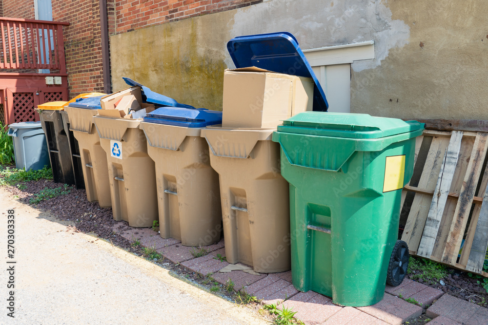 many trash and recycling bins loaded and waiting for pickup in an alley way many trash and recycling bins loaded and waiting for pickup in an alley way