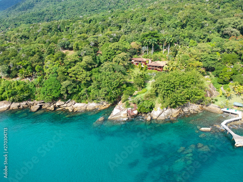 Aerial view of tropicsal house in forest surrounded by trees and next to the ocean and blue turquoise water. luxurious villa and spacious pavilion next to the sea  Brazil.