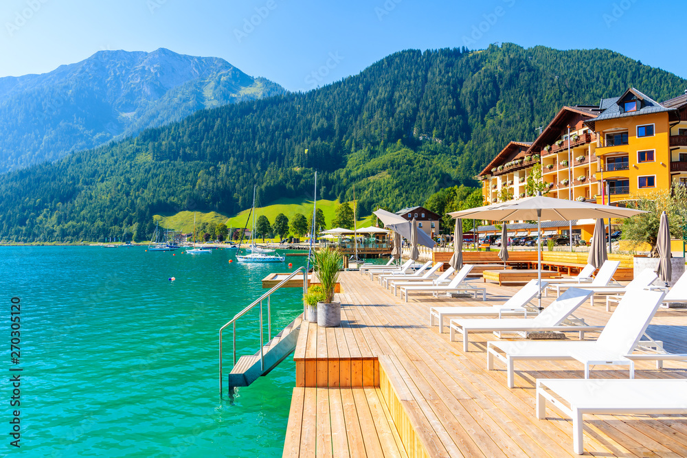 Pier with chairs on sunny terrace on shore of beautiful Achensee lake on sunny summer day with blue sky, Karwendel mountain range, Tirol, Austria