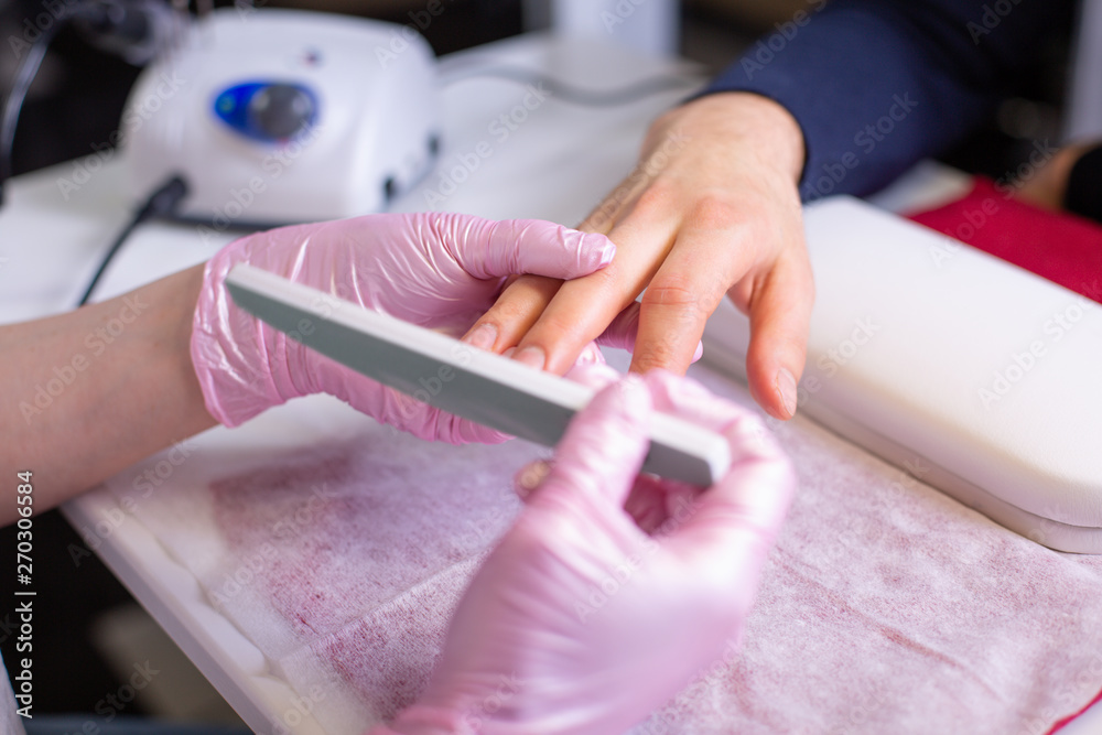 Fototapeta premium Professional manicure of male hands in a beauty salon close up. Master in gloves makes a manicure using modern technologies. Beauty concept of personal care, health, hand care.