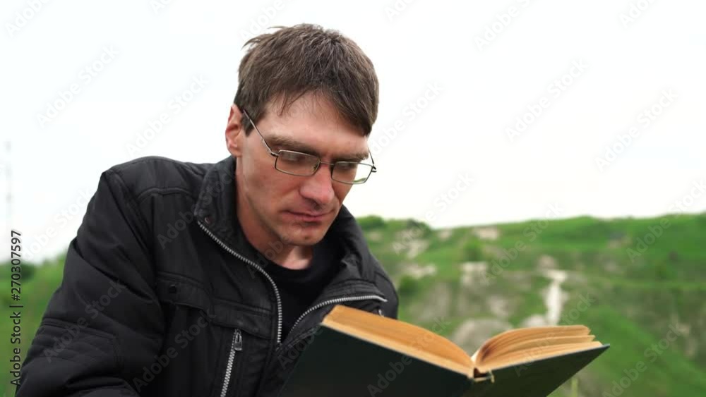 Man reading a book in nature. The concept of summer reading in nature, recreation with a book. The book is in the hands of a man. Man reading a book in nature. The concept of summer reading in nature, recreation with a book. The book is in the hands of a man.