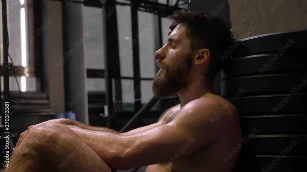 Closeup shoot of adult muscular athletic man sitting and being tired indoors in the gym