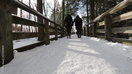 Two people walking down a snowy pathway. Snow covered ground with wooden railings in the dead of winter. photo