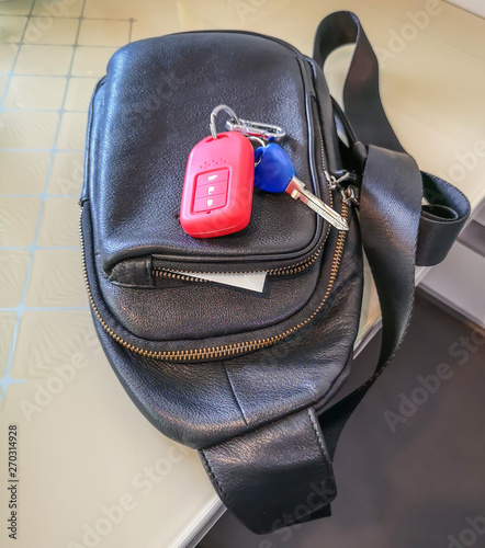 Car remote key wrapped in bright red silicone and men's bag placed on the table. photo