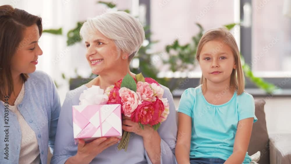 family, birthday greetings and three generations concept - portrait of smiling mother, daughter and grandmother with flowers and gift box at home family, birthday greetings and three generations concept - portrait of smiling mother, daughter and grandmother with flowers and gift box at home
