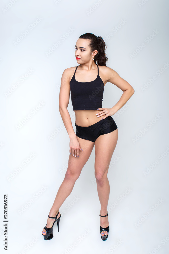 Fototapeta premium Beautiful girl in high heels in black clothes for dancing. Bare legs with smooth skin. Girl smiles.