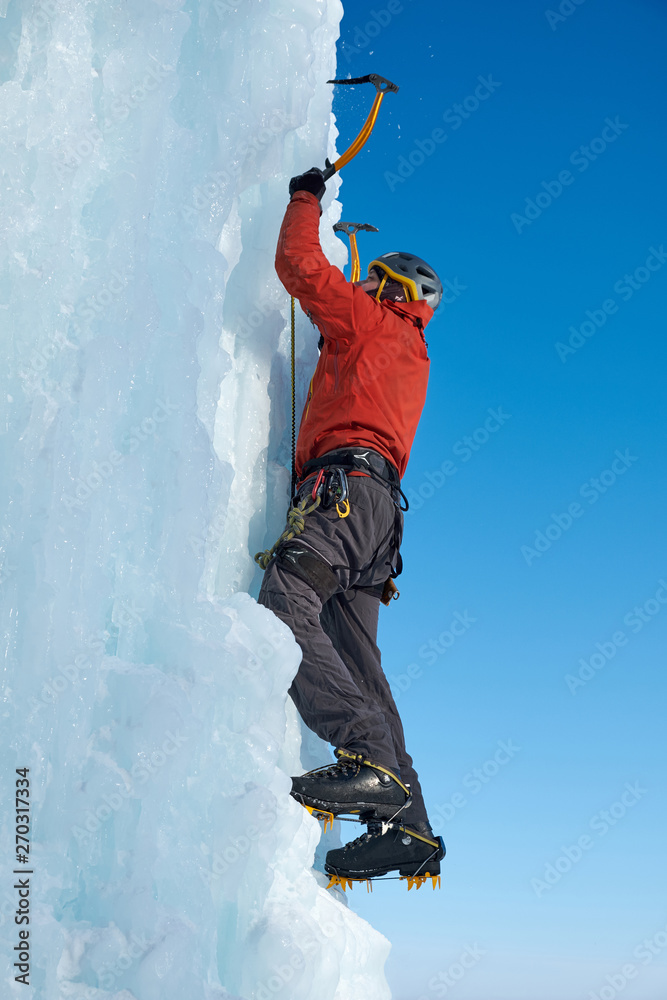 Alpinist man with ice tools axe climbing a large wall of ice. Outdoor Sports Portrait.