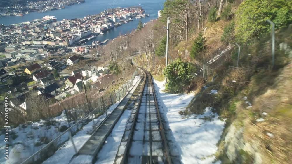 View out of the rear of a funicular train as it travels up Mount Fløyen with a view of Bergen in the distance View out of the rear of a funicular train as it travels up Mount Fløyen with a view of Bergen in the distance