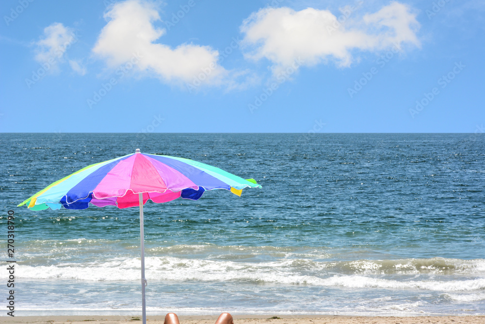 A colorful beach umbrella on the beach with a brigth blue sky an white fluffy clouds