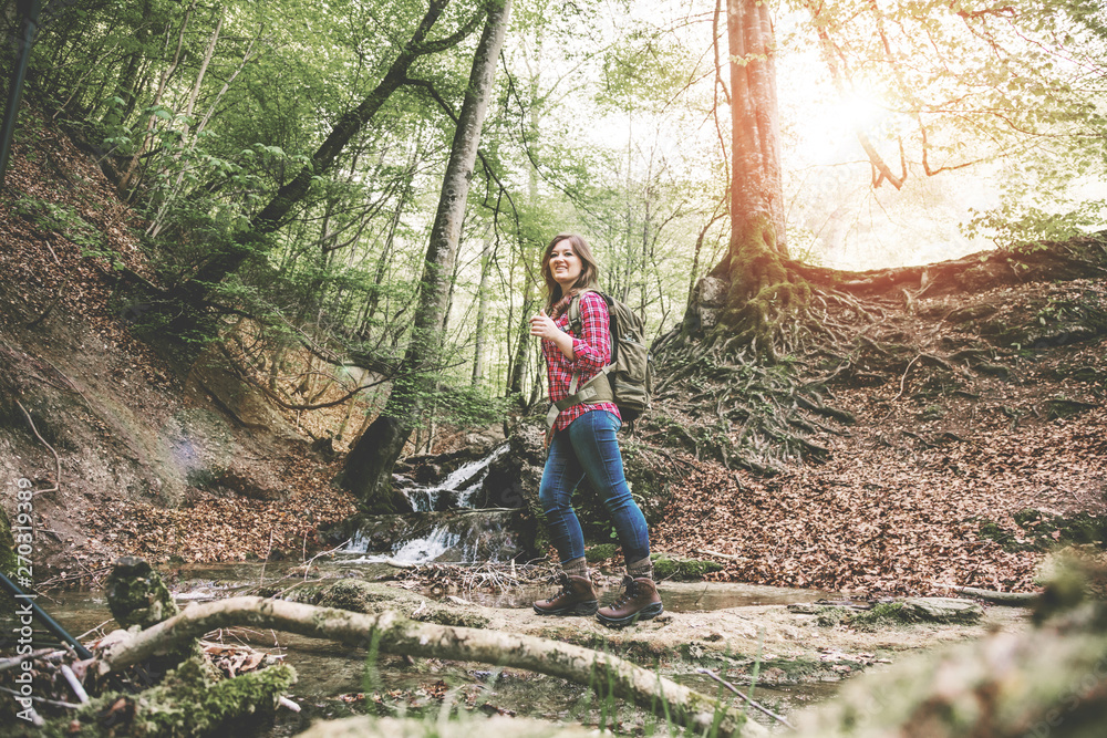 Naklejka premium Woman with backpack in a beautiful forest while hiking near a waterfall