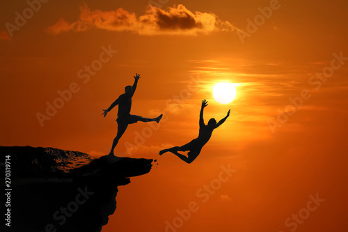 The concept of betrayal and the help of friends, Silhouette of Men are jumped between high cliff at a red sky sunset