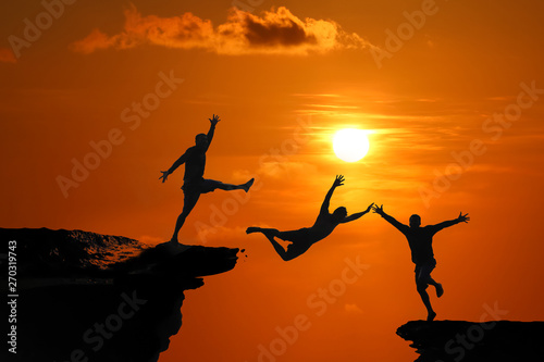 The concept of betrayal and the help of friends  Silhouette of Men are jumped between high cliff at a red sky sunset