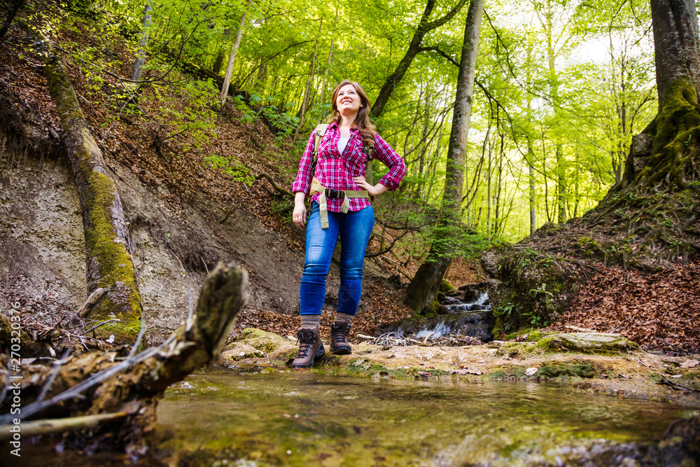Woman with backpack in a beautiful forest while hiking near a waterfall Woman with backpack in a beautiful forest while hiking near a waterfall