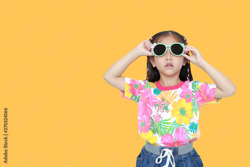 Cute little Asian kid girl wearing a flowers summer dress and sunglasses isolated on yellow background with copy space. Summer and fashion concept.