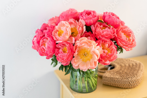 Coral peonies in a glass vase and wicker bag on wooden table.. Beautiful peony flower for catalog or online store. Floral shop concept . Beautiful fresh cut bouquet. Flowers delivery. Copy space