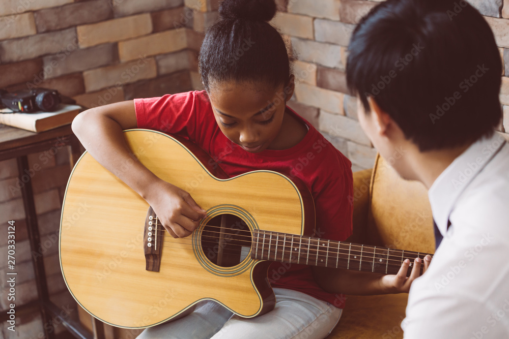 African American girl in casual outfit learning how to play guitar while  sitting on couch near male tutor during music lesson Stock Photo | Adobe  Stock