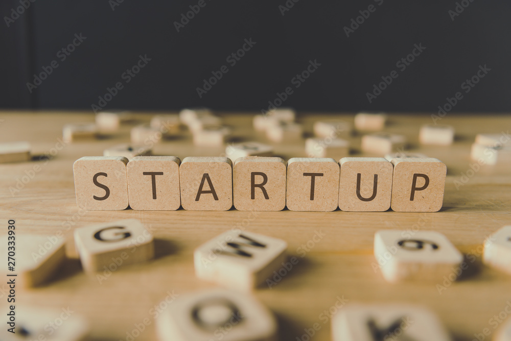 selective focus of startup inscription on cubes surrounded by blocks with letters on wooden surface isolated on black selective focus of startup inscription on cubes surrounded by blocks with letters on wooden surface isolated on black