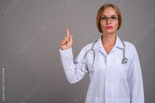 Young beautiful woman doctor with blond hair against gray backgr
