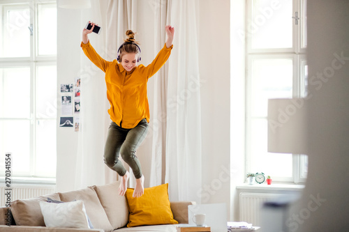 A young female student with headphones jumping on sofa when studying.