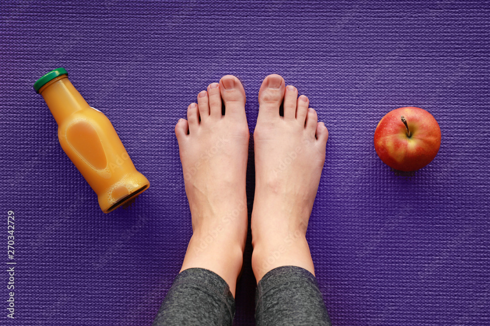 Naklejka premium Legs of sporty woman with apple and bottle of juice on yoga mat