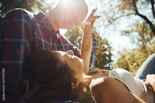Young romantic couple in love spend time in the park. Young woman lying on knees of man and looking at each other with sun rays background.