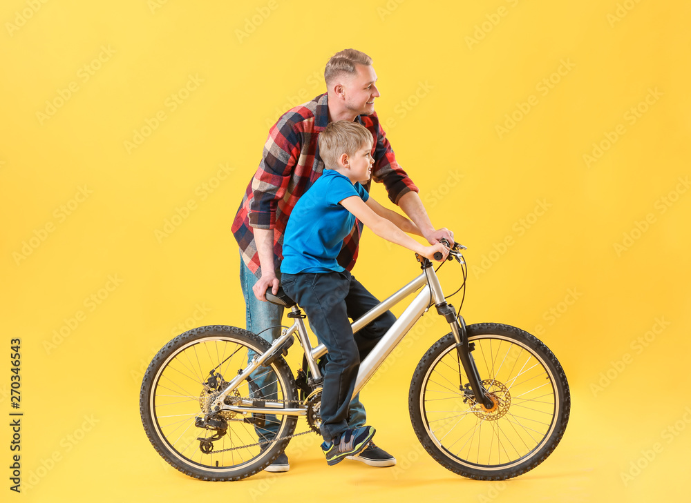 Father and his son with bicycle on color background Father and his son with bicycle on color background