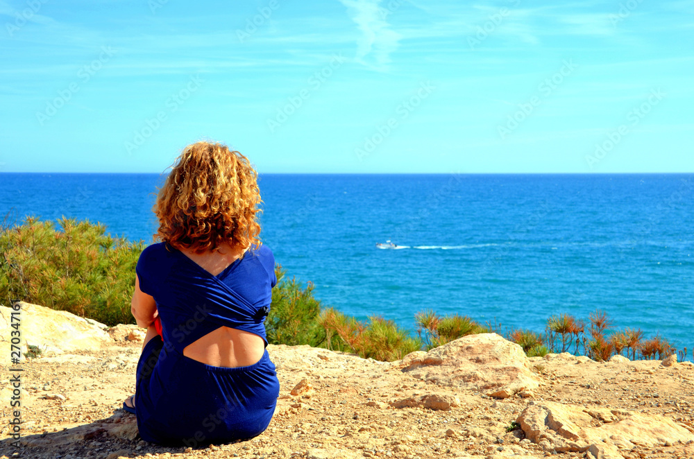 Blonde haired woman looking at the sea from the cliffs of torredembarra tarragona