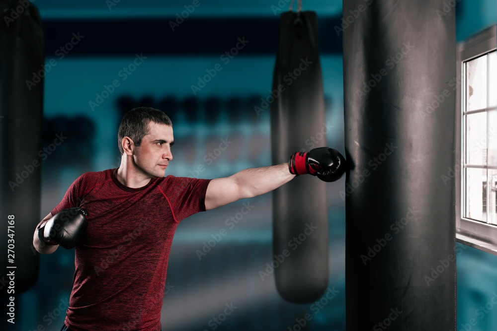 young short-haired man is training in a gym with a punching bag.