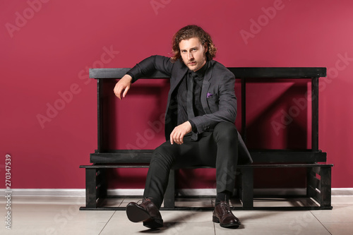Stylish young man sitting on bench near color wall © Pixel-Shot