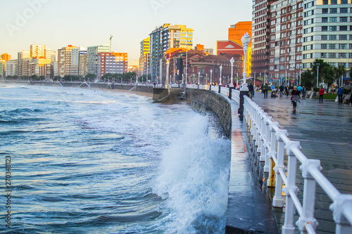 Waves splashing against the wall in San Lorenzo beach in Gijon, Asturias, Spain, with the promenade and buildings in one side photo