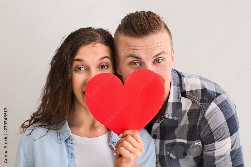 Adorable loving couple with paper heart on grey background