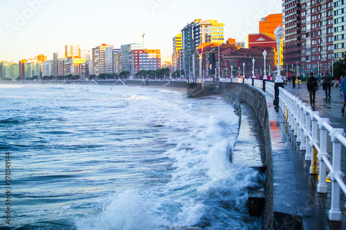 Waves crushing with the wall in San Lorenzo beach in Gijon, Asturias, Spain, with buildings and the promenade at the background