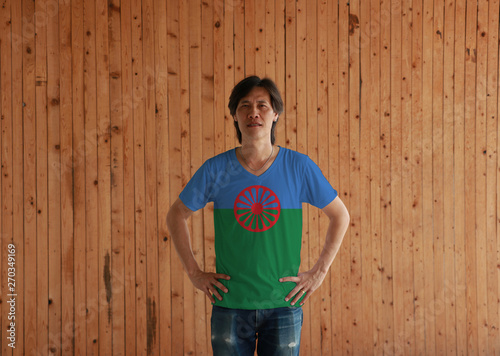Man wearing Romani people flag color shirt and standing with akimbo on the wooden wall background. Blue and green background.