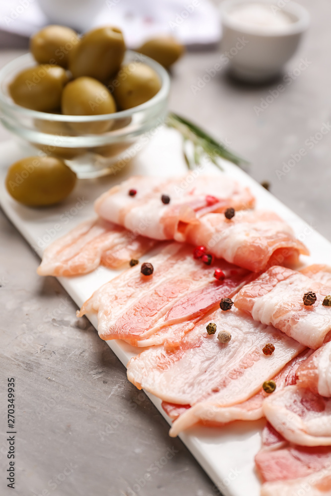 Board with fresh raw bacon and olives on table