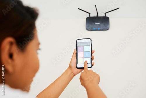 Young woman connecting wi-fi router with smartphone with smart home system application on the screen