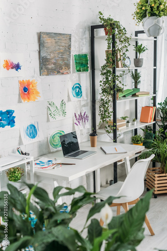 selective focus of selective focus of spacious room with laptop on table, paintings on wall and rack with potted plants © LIGHTFIELD STUDIOS