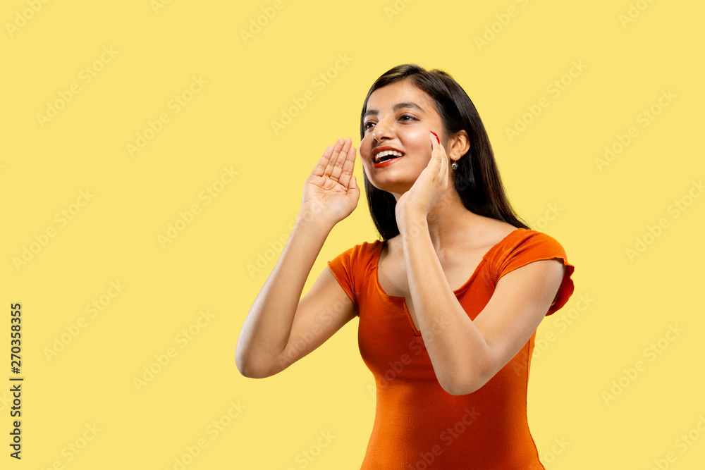Beautiful female half-length portrait isolated on yellow studio background. Young emotional indian woman in dress calling somebody. Negative space. Facial expression, human emotions, sales concept.