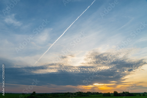 Beautiful evening sky with clouds during sunset. Trail from the plane on the background of a beautiful sky. Beautiful sky background during sunset