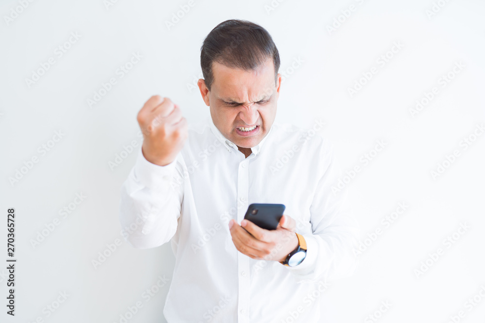 Middle age man using smartphone over white wall annoyed and frustrated shouting with anger, crazy and yelling with raised hand, anger concept Middle age man using smartphone over white wall annoyed and frustrated shouting with anger, crazy and yelling with raised hand, anger concept